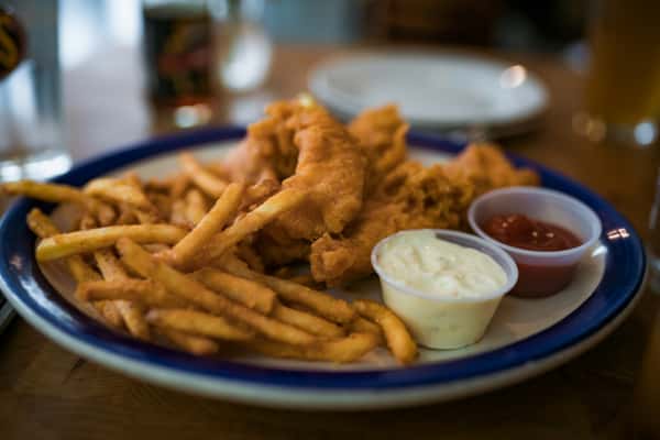 Crispy fried fish and chips served with golden fries, tartar sauce, and ketchup on a casual pub-style plate—classic comfort food meal.