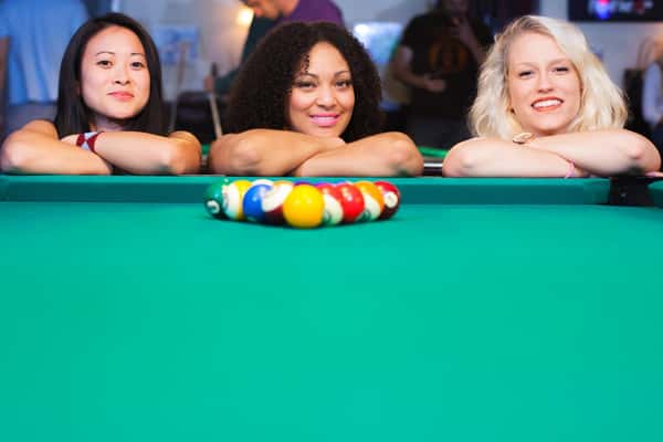 Three women leaning on pool table