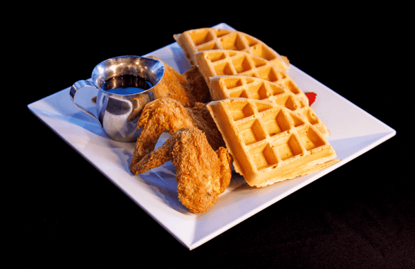 Delicious chicken and waffles served at Neil St. Blues in Champaign, IL, featuring crispy fried chicken wings and golden-brown waffles with a side of syrup.