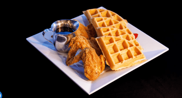 "Delicious chicken and waffles served at Neil St. Blues in Champaign, IL, featuring crispy fried chicken wings and golden-brown waffles with a side of syrup."