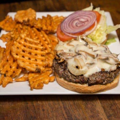 open faced cheeseburger topped with mushrooms and a side of fries