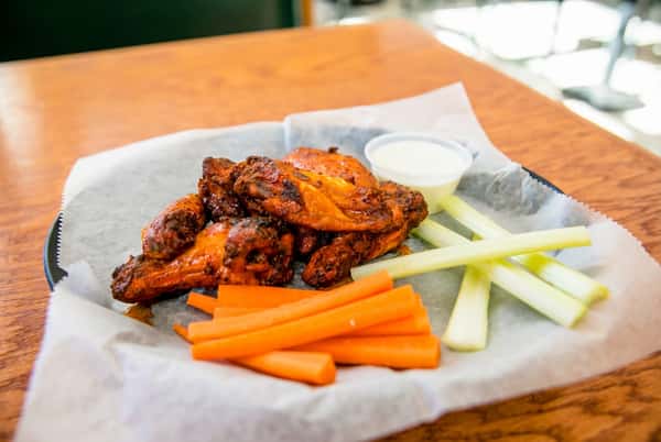 Chicken wings with ranch dipping sauce, carrot sticks, and celery sticks in a basket lined with paper.