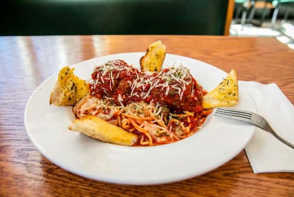 Spaghetti and meatballs with red sauce, shredded cheese, and garlic bread on a white plate.