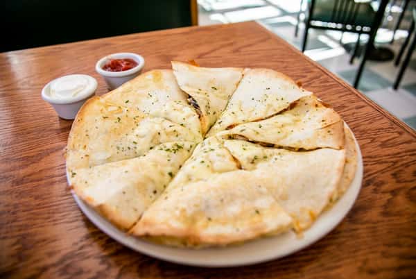 Cheese quesadilla with melted cheese, served with sides of white sour cream and red salsa on a wooden table.