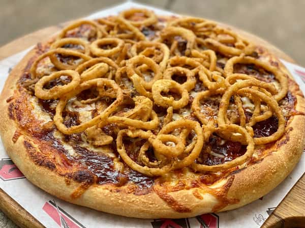 BBQ chicken pizza with melted mozzarella cheese, drizzled with brown BBQ sauce, and topped with crispy fried onion rings.