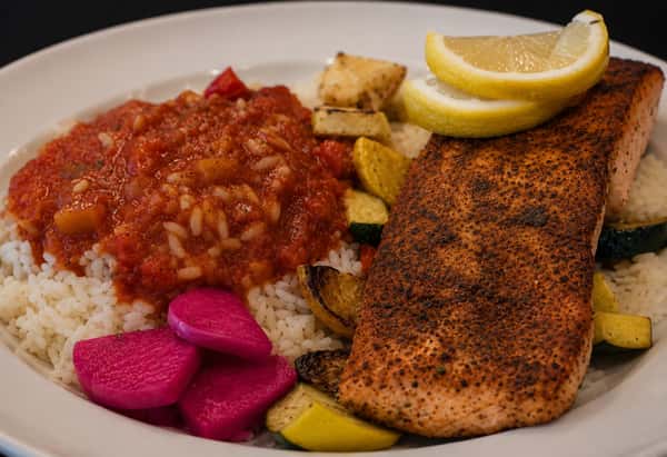 Cajun-seasoned salmon served with tomato rice, roasted vegetables, lemon, and pickled turnips