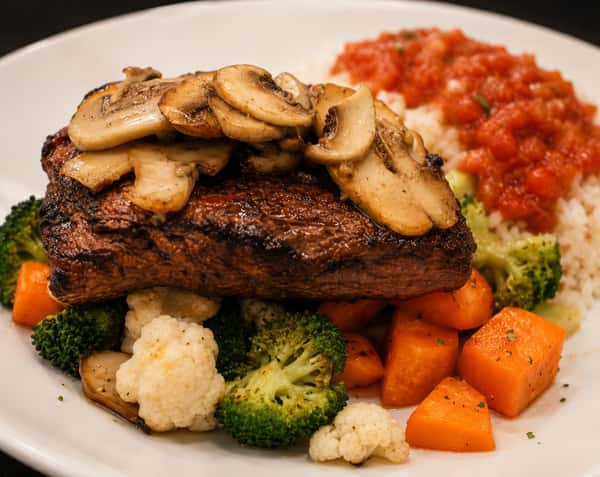 Grilled sirloin steak topped with sautéed mushrooms and served with rice and vegetables