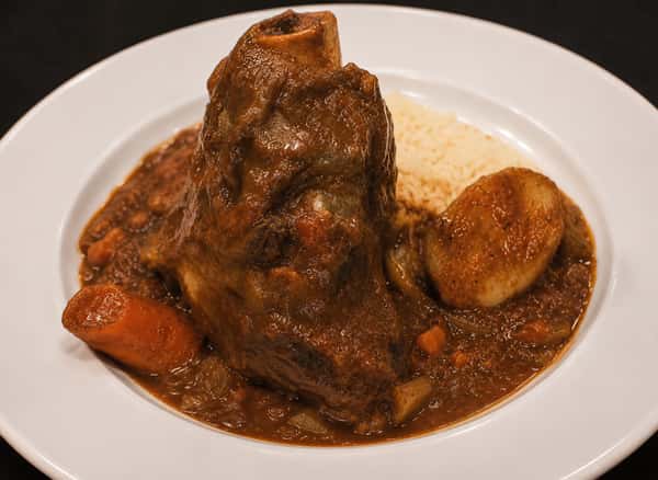 Braised lamb shank served in a savory sauce with potatoes and carrots