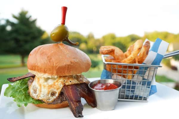 burger topped with bacon and a fried egg with french fries and ketchup on the side.