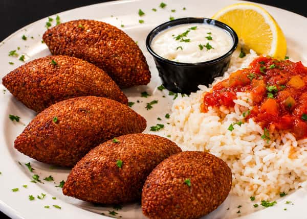 Fried kibbeh balls served with rice, tomato sauce, yogurt dip, and pickled turnips