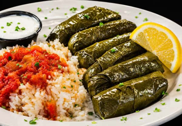 Stuffed grape leaves served with rice, tomato sauce, yogurt dip, and lemon
