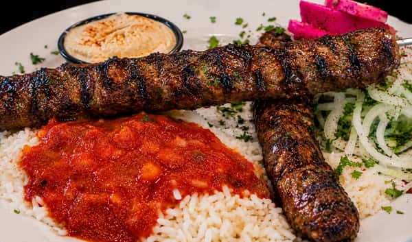 Grilled kafta kebabs served with rice, tomato sauce, onions, pickled turnips, and tahini