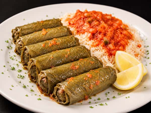 Stuffed grape leaves served with tomato rice, lemon wedges, and fresh herbs
