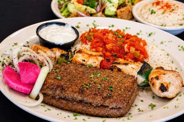 Baked kibbeh served with rice, grilled chicken, tomato sauce, onions, pickled turnips, and dipping sauces
