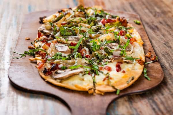 A flatbread style pizza topped with arugula and roasted vegetables