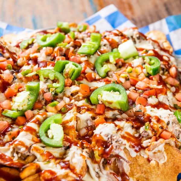 A nacho platter toped with jalapeno and BBQ sauce