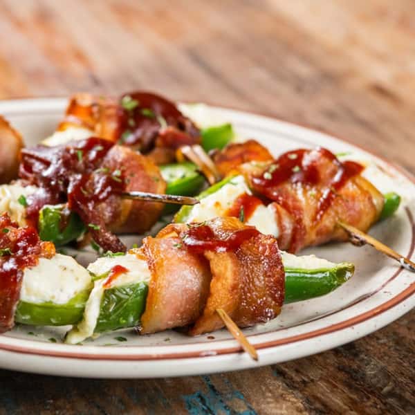 Cheese stuffed peppers wrapped in bacon with a sauce drizzled on top