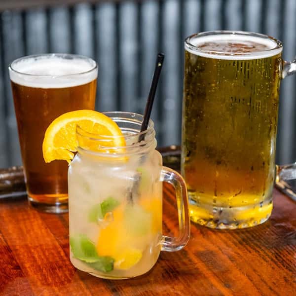 A lemon cocktail and two glasses of beer on the bar countertop