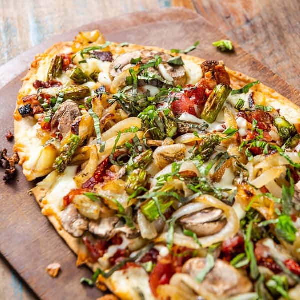 A flatbread style pizza topped with arugula and roasted vegetables