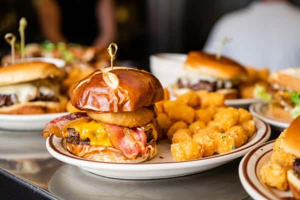 A plate with a bacon cheeseburger and tater tots on the side