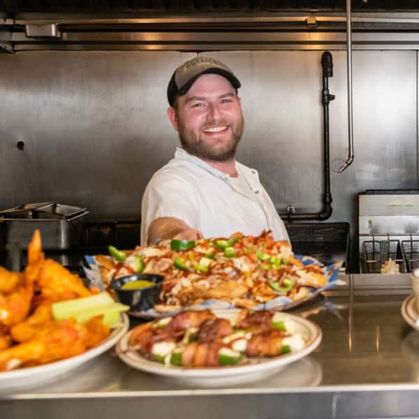 The chef smiling with multiple plates of entrees in front of him