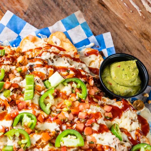 A nacho platter toped with jalapeno and BBQ sauce