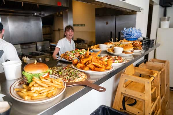 Multiple plates filled with different menu items such as fried fish, flatbread pizzas and burgers