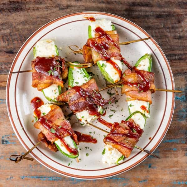 Cheese stuffed peppers wrapped in bacon with a sauce drizzled on top
