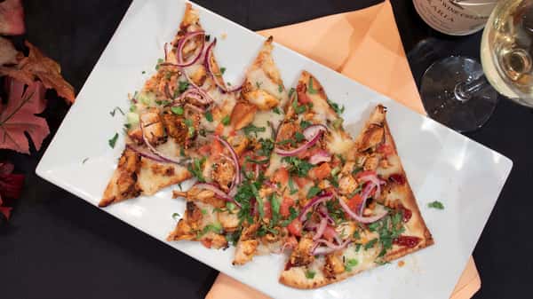 A tray of loaded nachos topped with melted cheese, diced tomatoes, onions, fresh herbs, and savory toppings. The dish is colorful and vibrant, perfect for sharing as a flavorful appetizer or bar-style snack.