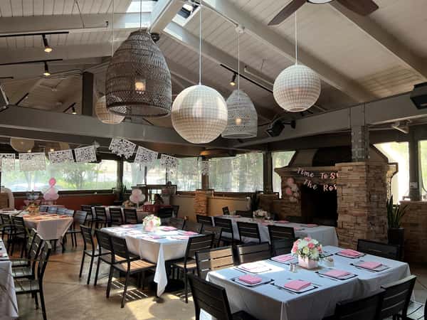 Light-filled restaurant venue prepared for a baby shower or bridal event, with soft pink napkins, white tablecloths, delicate floral centerpieces, and papel picado banners enhancing the cozy atmosphere.