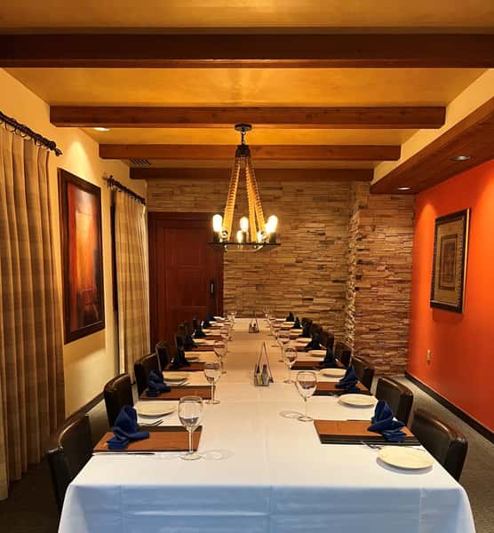 Long banquet table in a cozy private room with stone walls, wood beams, and navy napkins.