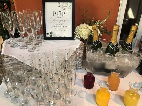 Bridal shower mimosa bar with champagne, fruit juices, and flutes on ice.