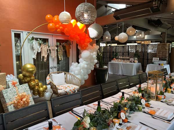 Whimsical table with greenery, orange-themed decor, and a balloon arch over a cozy chair.