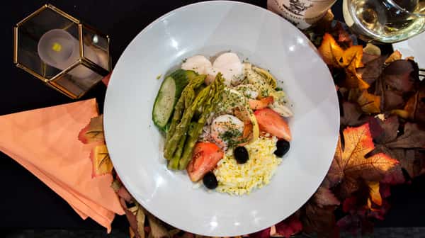 A vibrant plate of gourmet pasta topped with grilled salmon, asparagus, and fresh herbs. The dish is finished with grated cheese and a light sauce, creating a colorful and elegant presentation that highlights fresh ingredients and refined flavors.