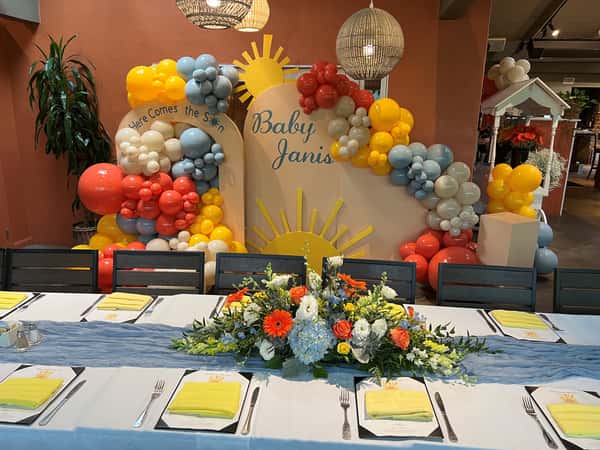 Sunshine-themed baby shower backdrop with balloon garlands and a vibrant floral centerpiece.