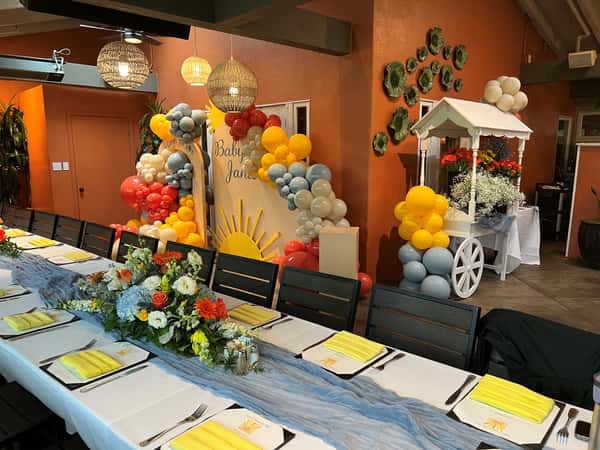 Colorful baby shower setup with a sunshine theme, pastel balloons, floral centerpiece, and yellow napkins.