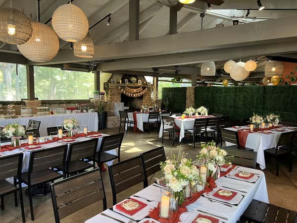 Chic event dining area in a restaurant decorated with ivory and peach florals, amber candles, and rust-colored table runners, under woven pendant lighting and surrounded by lush greenery walls.