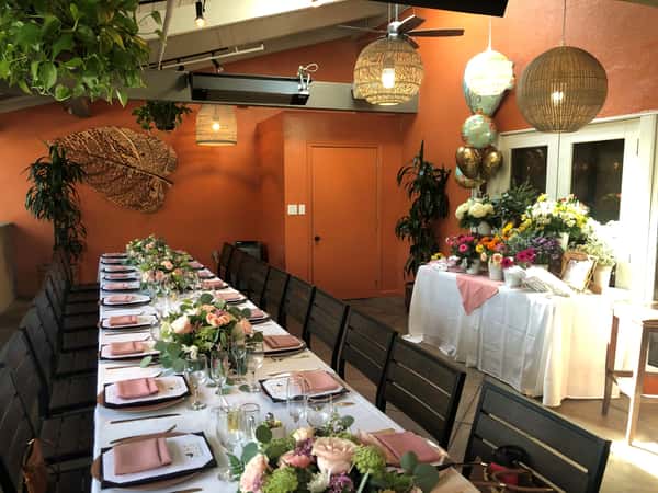 Romantic event table with blush napkins, pastel florals, and rustic orange walls in a bright venue space.