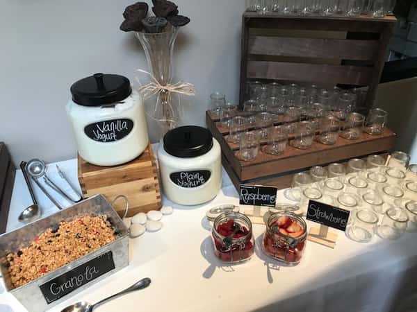 Yogurt station with granola and fruit options next to shotglasses.