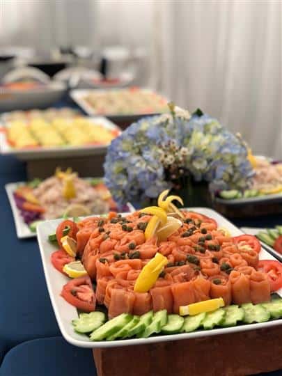 Salmon with capers on dish garnished with tomatoes, lemons, cucumbers.