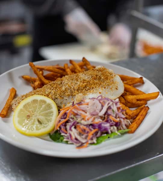 A crispy breaded fish fillet served with golden French fries, creamy coleslaw, and a lemon wedge for a classic seafood meal.