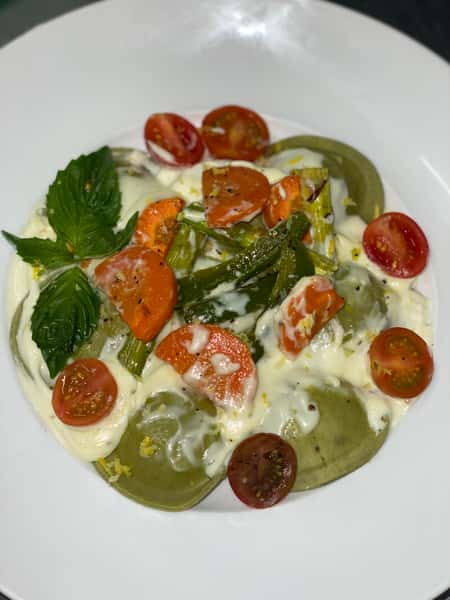 A fresh caprese-style salad made with sliced heirloom tomatoes, creamy mozzarella, basil leaves, cherry tomatoes, and a drizzle of pesto and olive oil.