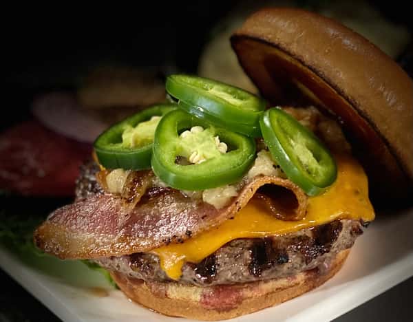 A close-up of a juicy cheeseburger topped with fresh jalapeño slices, featuring a perfectly seared beef patty, melted cheddar cheese, and a toasted bun.