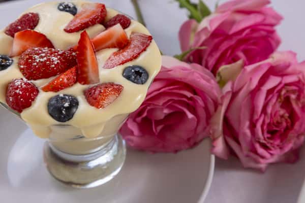 Italian dessert topped with fresh strawberries and blueberries beside pink flowers