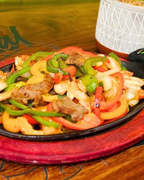 Sizzling fajita mix of grilled steak, chicken, shrimp, and bell peppers on a cast iron skillet.