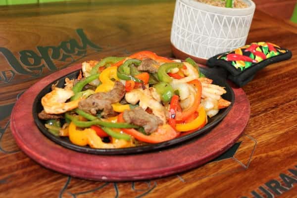 Sizzling fajita platter with shrimp, beef, and chicken, sautéed with colorful bell peppers and onions, served on a hot cast iron skillet.