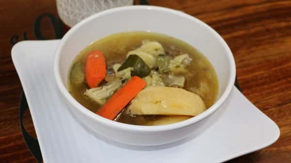Beef bone soup with carrots, potatoes, and cabbage served with chopped onions, jalapeños, cilantro, and lime wedges.