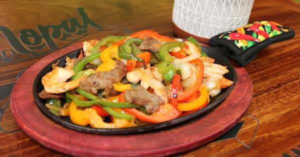 Sizzling fajita platter with shrimp, beef, and chicken, sautéed with colorful bell peppers and onions, served on a hot cast iron skillet.
