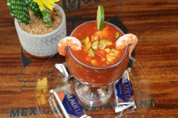 Shrimp cocktail in tomato-based sauce with avocado and lime, garnished with shrimp and served with saltine crackers.