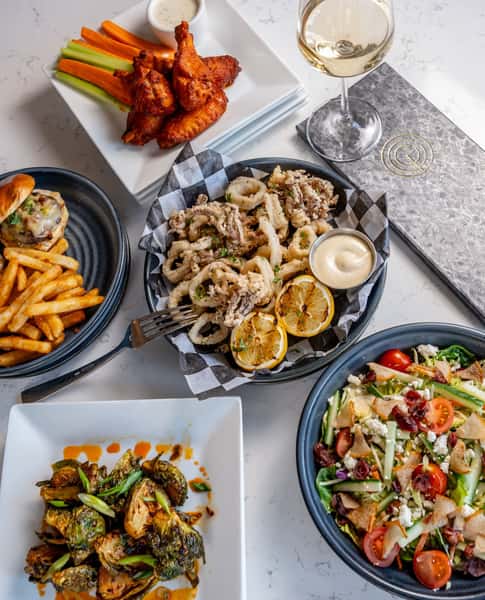 Plates of burgers, fried calamari, chicken wings and salad on a table